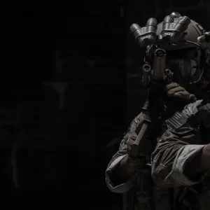 Soldiers in multicam uniforms with night vision and suppressed rifles clearing a dark room