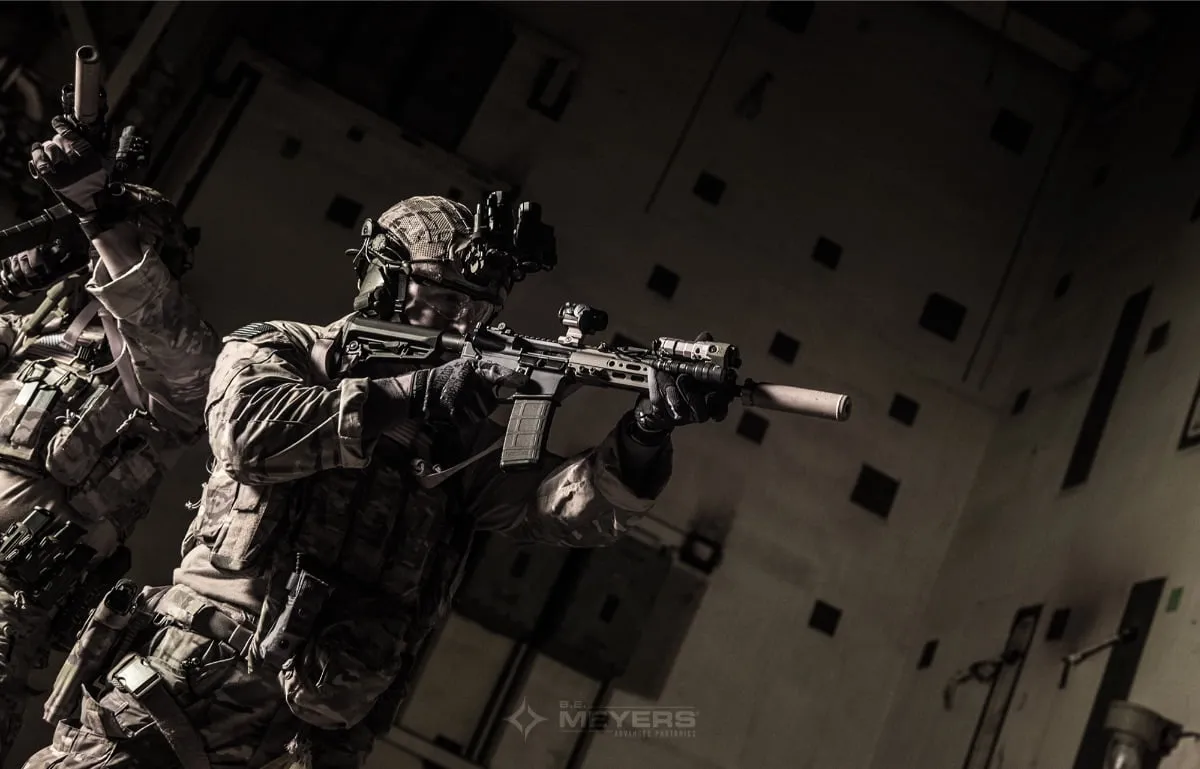 Soldiers in multicam uniforms with night vision and suppressed rifles clearing a dark room